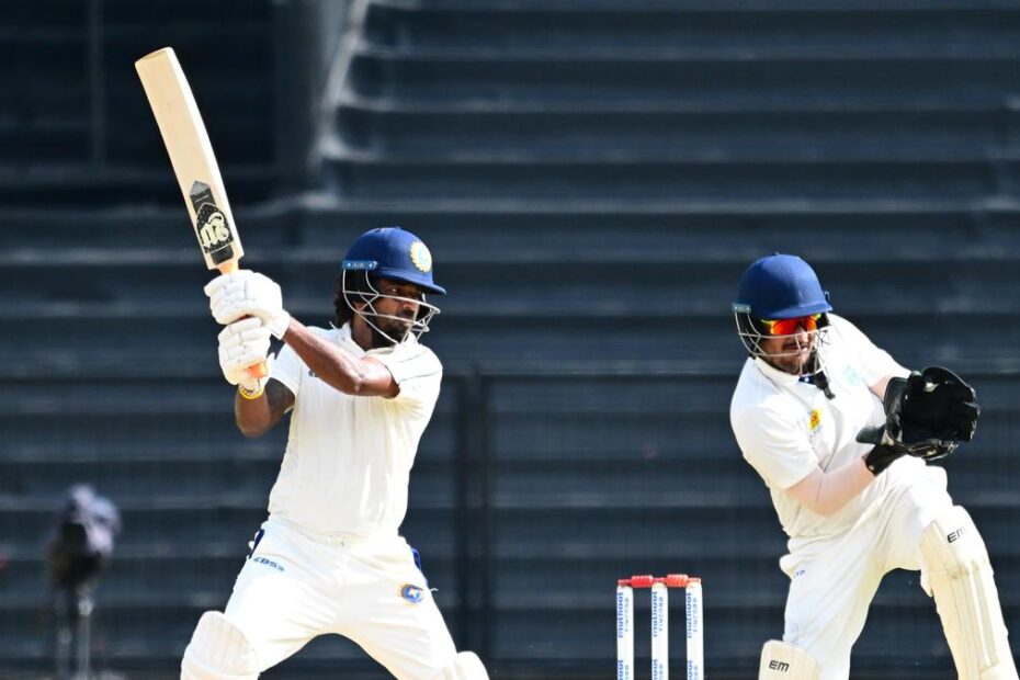 Odisha vs Services Match Two cricket players in white at the crease; left batter swings the bat while a teammate prepares to field near the wickets. Indibet Betting and Casino