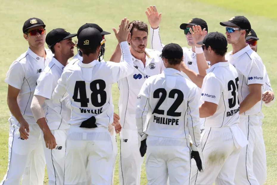 Western Australia vs New South Wales Cricketers in white uniforms celebrate on a grass field, high-fiving each other in a team huddle. Indibet Betting and Casino